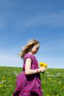 Menina carregando flores silvestres no campo — Fotografia de Stock