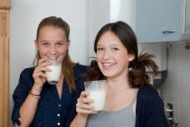 Улыбающиеся девушки пьют молоко на кухне, сосредотачиваются на переднем плане — стоковое фото