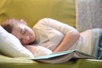 Jovem deitada no sofá, com livro — Fotografia de Stock