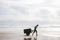 Человек на пляже тянет корзину на закате — стоковое фото