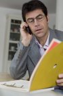 Mature man working at home and using mobile phone — Stock Photo