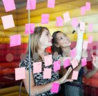 Businesswomen sticking pink notes on window, selective focus — Stock Photo