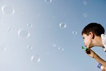 Мальчик, дующий пузырьками на голубое небо — стоковое фото