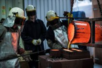 Male foundry workers pouring bronze melting pot in bronze foundry — Stock Photo