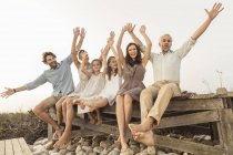 Portrait of two girls and adults sitting on boardwalk with arms raised, Grotto Bay, South Africa — Stock Photo