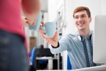 Woman giving to young man coffee in office — Stock Photo