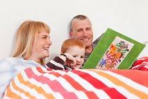 Family reading book together in bed — Stock Photo
