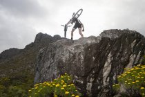 Joven llevando bicicleta de montaña en la cima de la formación de rocas - foto de stock