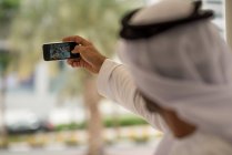 Mais de ombro do homem do Oriente Médio levando selfie smartphone com amigos no café, Dubai, Emirados Árabes Unidos — Fotografia de Stock