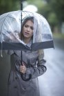 Mujer joven mirando el agujero en el paraguas - foto de stock