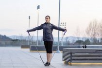 Jovem mulher se exercitando ao ar livre, usando corda de alongamento — Fotografia de Stock