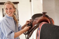 Woman smiling picking up saddle — Stock Photo