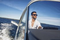 Young man in sunglasses steering boat — Stock Photo