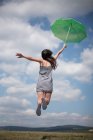 Visão traseira da mulher adulta média segurando guarda-chuva verde, saltando — Fotografia de Stock