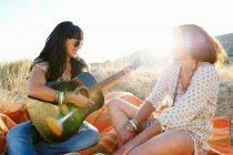 Women playing guitar in grass — Stock Photo