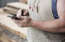 Carpinteiro em avental usando telefone celular, close-up vista parcial — Fotografia de Stock