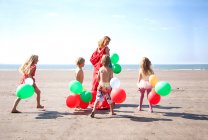 Madre con cuatro hijos en la playa con globos, Gales, Reino Unido - foto de stock