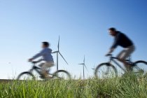 Père et fils faisant du vélo devant un parc éolien — Photo de stock