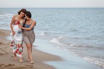 Women walking along shore with arm around, one pregnant — Stock Photo