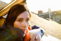 Woman with cup leaning out of window — Stock Photo