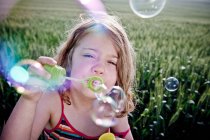 Girl blowing bubbles to camera — Stock Photo