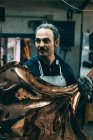 Métallurgiste tenant un produit en cuivre dans un atelier de forge — Photo de stock