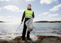 Lavoratore in giubbotto di sicurezza pulizia spiaggia — Foto stock