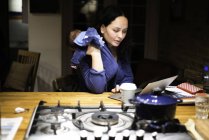 Mutter wiegt neugeborenen Sohn und benutzt Laptop auf Küchentisch — Stockfoto