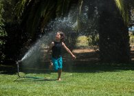 Хлопчик біжить крізь воду з садового спринклера — стокове фото