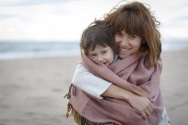 Mère et fille enveloppées dans une couverture étreignant sur la plage — Photo de stock