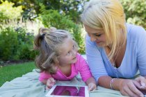 Мати і дочка лежать на ковдрі в саду за допомогою цифрового планшета — стокове фото
