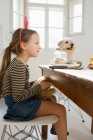 Mädchen und Hund sitzen am Tisch in Küche — Stockfoto