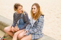 Подружки сидять на стіні на пляжі — стокове фото
