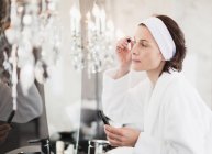 Woman in bathrobe applying makeup — Stock Photo