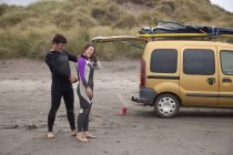 Man helping woman putting wet suit on beach — Stock Photo