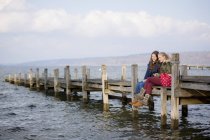 Две девочки-подростки сидят на деревянной пристани — стоковое фото