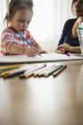 Criança feminina à mesa com a mãe desenhando em caderno de esboços — Fotografia de Stock
