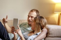 Середня доросла пара розслабляється на дивані, дивлячись на цифровий планшет — стокове фото