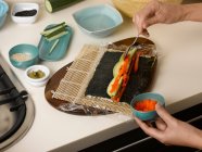 Imagem recortada de Mulher preparando rolo de sushi à mesa — Fotografia de Stock