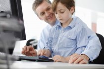 Menino sentado no colo do pai usando o teclado do computador — Fotografia de Stock