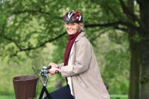 Senior woman riding bicycle in park, portrait — Stock Photo