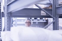 View through shelves of factory worker looking at camera — Stock Photo
