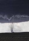 Tornado delgado con nube de embudo aterriza sobre pradera rural - foto de stock