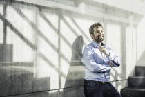 Selbstbewusster Geschäftsmann lehnt im Büro-Treppenhaus an Wand und lächelt — Stockfoto