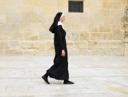 Nun walking in front of stone wall — Stock Photo