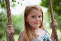 Smiling girl sitting in tree swing, focus on foreground — Stock Photo