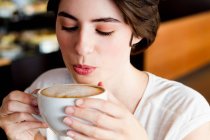 Woman blowing on coffee in cafe — Stock Photo