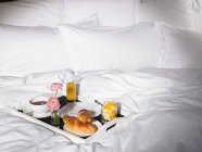 Поднос для завтрака с чашкой кофе и круассанами в постели — стоковое фото