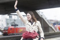 Young woman using wheelchair waving from city train station — Stock Photo