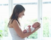 Mother holding infant son by window — Stock Photo